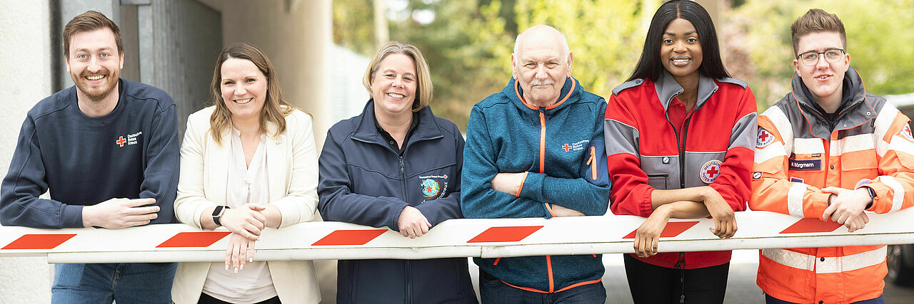 sechs DRK Mitarbeiter aus verschiedenen Bereichen posieren vor Schranke